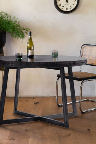 The Stylish Mango Wood Round Dining Table styled with a chair, plant and clock, with a wine bottle and some glasses on.