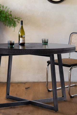 The Stylish Mango Wood Round Dining Table with a wine bottle and glasses on, styled with a dining chair and plant.