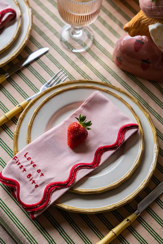 Beautiful pale pink napkin with red scalloped edge on a dinnerware placesetting.