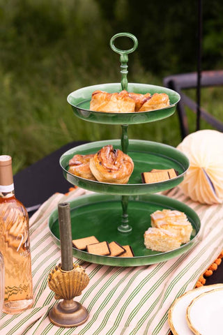 The Fresh Green Large Enamel Tiered Serving Tower styled on an outdoor table with pastries and biscuits, displayed with various other accessories.