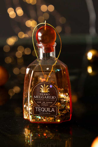 The Tequila Christmas Tree Decoration styled on a dark surface with lights in the background.