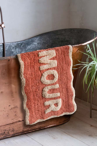 The Terracotta Amour Bath Mat displayed over the edge of a copper bath, styled with a plant.