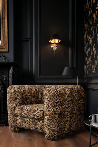 The Bowie Love Seat In Leopard Love Velvet Natural styled in the corner of a dark room, with a wall light illuminated on the wall behind.