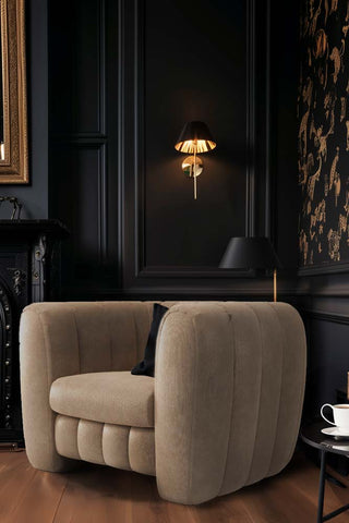 The Bowie Love Seat In Luxe Needlecord Velvet Natural Whisper styled in the corner of a dark living room, with a light on in the background.