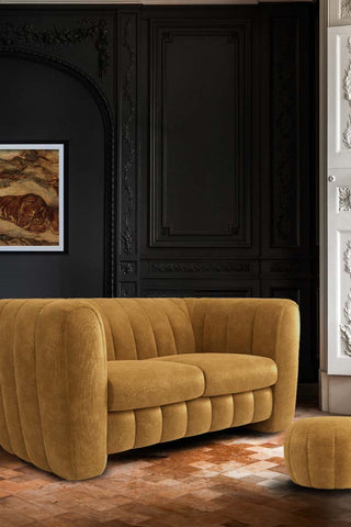 The Bowie Medium Sofa In Luxe Needlecord Velvet Golden Glow styled in front of a dark wall with an art print on, with a matching footstool.