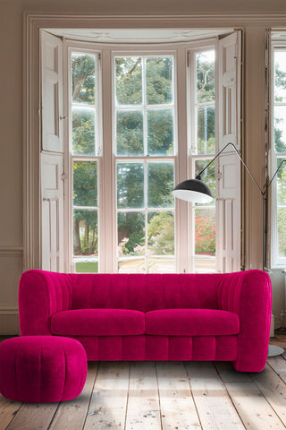 The Bowie Medium Sofa In Luxe Needlecord Velvet Harry's Pink styled in front of a large window, with a matching footstool and a floor lamp.