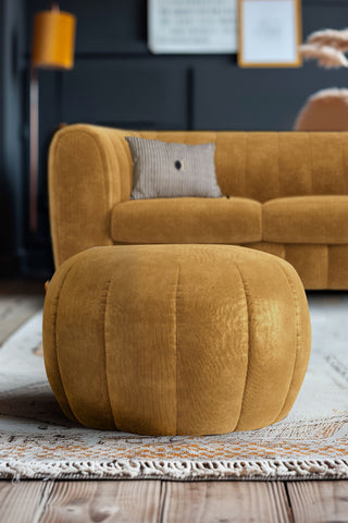 The Bowie Stool In Luxe Needlecord Velvet Golden Glow on a rug in a living room, with the matching sofa in the background.