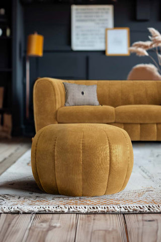 The Bowie Stool In Luxe Needlecord Velvet Golden Glow styled on a rug in a living room, in front of the matching sofa.