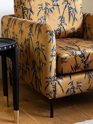 Close-up of the The Edie Bamboo & Golden Glow Velvet Armchair styled next to a side table.