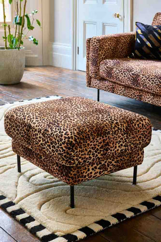 The Grace Foot Stool In Leopard Love Velvet Natural styled in a living room on a rug.