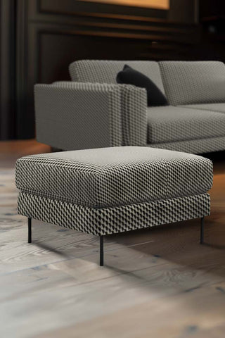 The Grace Foot Stool In Geo Glam Woven Sand & Black styled on a wooden floor, next to the matching sofa.