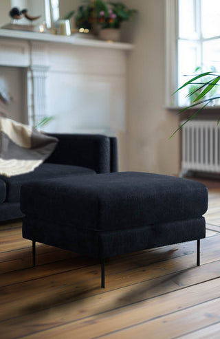 The Grace Foot Stool In Luxe Needlecord Velvet Midnight Navy styled in a living room in front of the matching sofa.