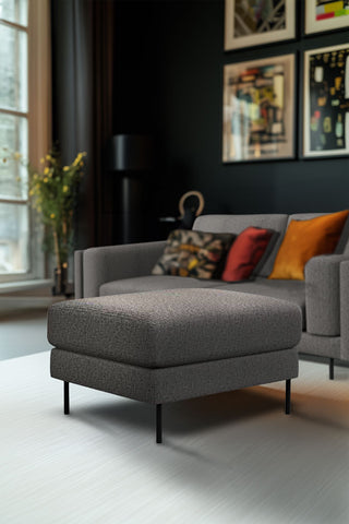 The Grace Foot Stool In Timeless Texture Black Bean styled in a living room in front of the matching sofa.