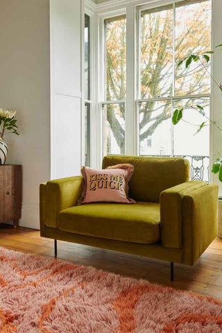 The Grace Love Seat In Luxe Kneedlecord Velvet Vintage Green styled in a living room in front of a window, with a cushion on.