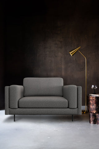 The Grace Love Seat In Timeless Texture Black Bean styled in front of a dark wall with a floor lamp, side table, book and glass.