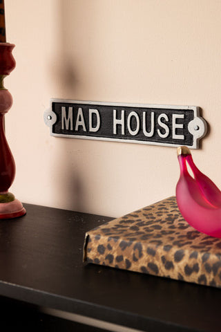 The Madhouse Sign styled on a wall above a leopard print notebook, banana ornament and a colourful candlestick holder.