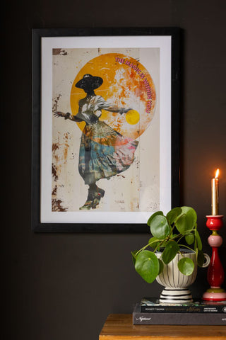 The Magic Is Within You Art Print displayed on a black wall, styled above a plant in a pot, books and a lit candle in a candlestick holder.