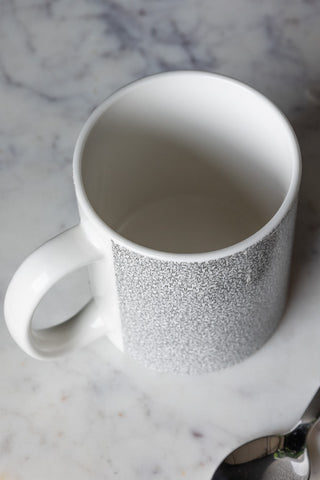 Close-up of The Micro Penis Mug on a marble surface with a spoon, seen from above.