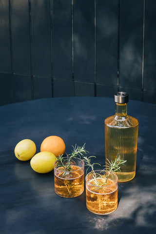 The Paveau - Gorgeous Ribbed Glass Carafe in Amber styled on a blue table with two drinks and some fruit.