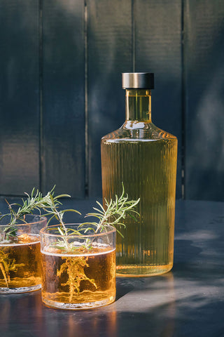 The Paveau - Gorgeous Ribbed Glass Carafe in Amber styled on a table with two drinks, in front of a blue tiled wall.