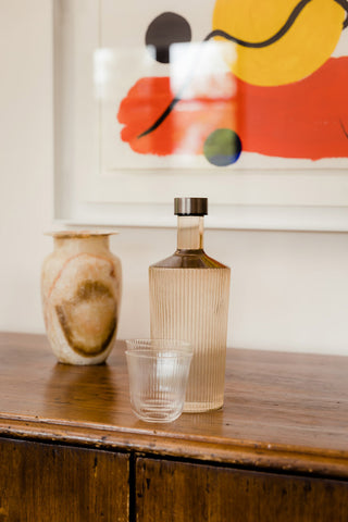 The Paveau - Gorgeous Ribbed Glass Carafe in Amber styled on a wooden sideboard with glasses and a vase.