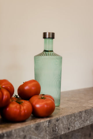 The Paveau - Gorgeous Ribbed Glass Carafe in Green styled on a ledge with tomatoes.