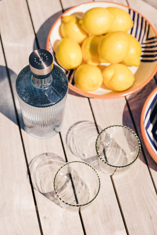 The Paveau - Gorgeous Ribbed Glass Carafe in Grey Blue styled on an outdoor table with glassware, bowls and lemons.