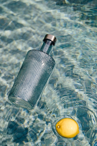 The Paveau - Gorgeous Ribbed Glass Carafe in Grey Blue floating in water with a lemon.