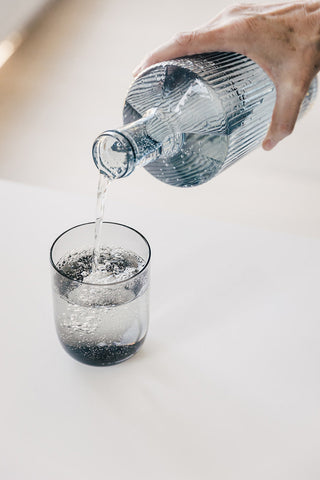 The Paveau - Gorgeous Ribbed Glass Carafe in Grey Blue pouring water into a glass.