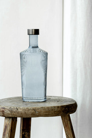 The Paveau - Gorgeous Ribbed Glass Carafe in Grey Blue styled on a wooden stool.