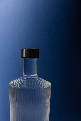 The Paveau - Gorgeous Ribbed Glass Carafe in White styled in front of a blue wall.