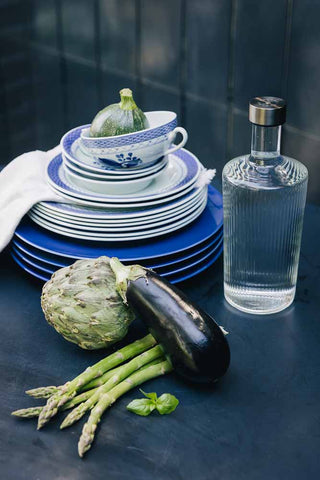 The Paveau - Gorgeous Ribbed Glass Carafe in White styled on a table with plates and vegetables.