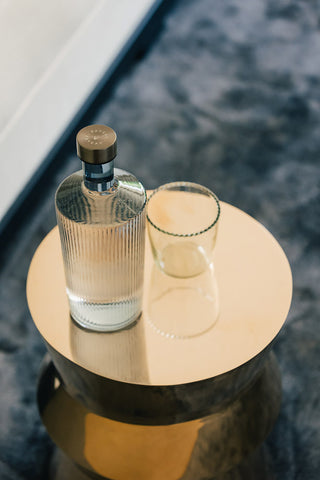 The Paveau - Gorgeous Ribbed Glass Carafe in White styled on a side table with a glass.