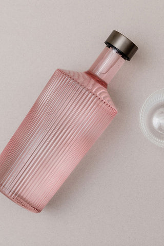 The Paveau - Gorgeous Ribbed Glass Carafe in Pale Pink laying on its side, styled next to a glass.