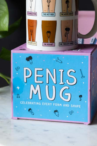 The Penis Mug displayed on its box on a marble table.