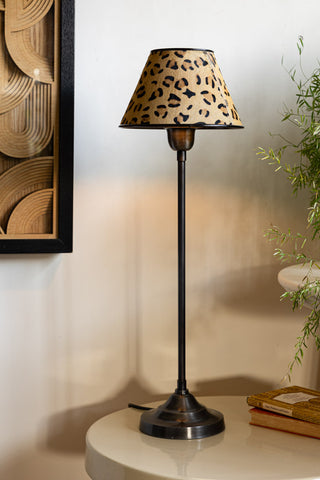 The Thin Table Lamp With Leopard Shade displayed on a table, styled with home accessories and a plant.