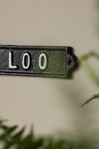 The Toilet Door Hanging Sign on the wall with a plant also in shot.