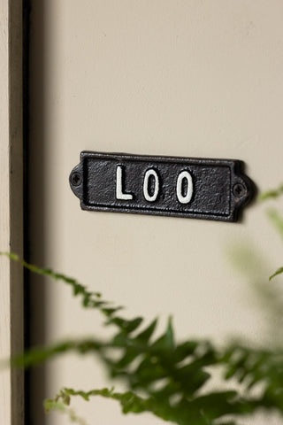 The Toilet Door Hanging Sign displayed on a neutral wall with a plant also in shot.