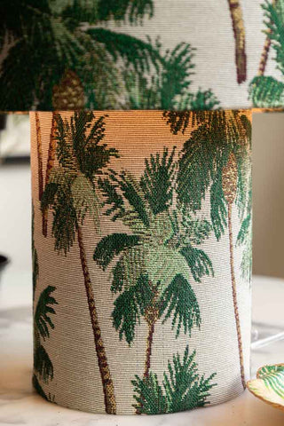 The base of the Green Palm Tree All-Fabric Table Lamp. The lamp is lit and there are palm trees repeated on the fabric.