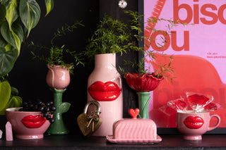 A very colourful Valentine's display of love related products including, pink and red lips vases, bowls and mugs, a love locket, flower vases and a pink bisou print.