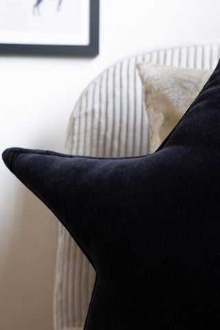 Close-up of the Velvet Star Cushion In Black on a chair with another cushion.