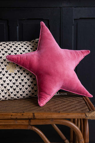 The Velvet Star Cushion In Hot Pink displayed on a bench with another cushion, in front of a black wall.