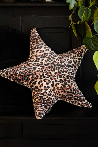 The Velvet Star Cushion In Leopard Print styled on a black bench next to a hanging green plant.