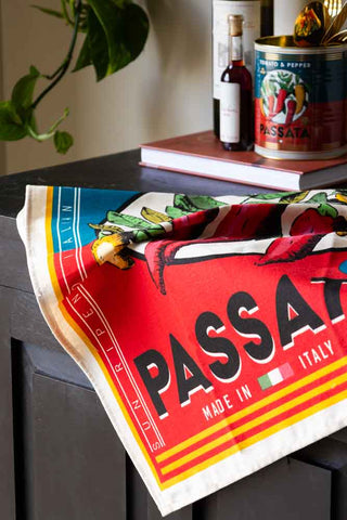 The Vintage Passata Tea Towel styled on the edge of a sideboard with kitchen accessories and a plant in the background.