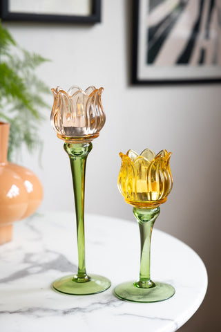 The Vintage-Style Yellow Glass Flower Candle Holder together with the orange version, displayed on a white table.