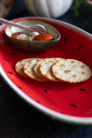 A close up of the Lifestyle image of the Watermelon Serving Plate with crackers and bowl ontop