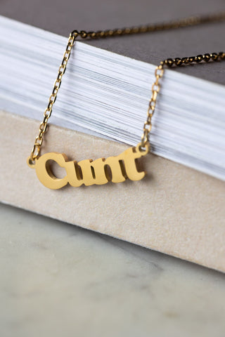 The Waterproof Gold Cunt Necklace styled on the corner of a neutral surface.