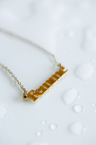 The Waterproof Gold Femme Necklace styled on a white surface with water droplets.