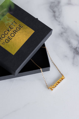 The Waterproof Gold Femme Necklace styled on a white marble surface with the box.