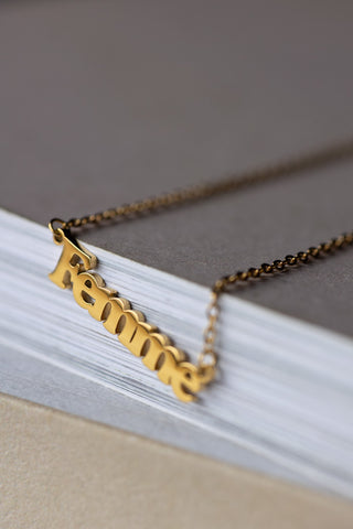 Close-up of the Waterproof Gold Femme Necklace on the corner of a neutral surface.